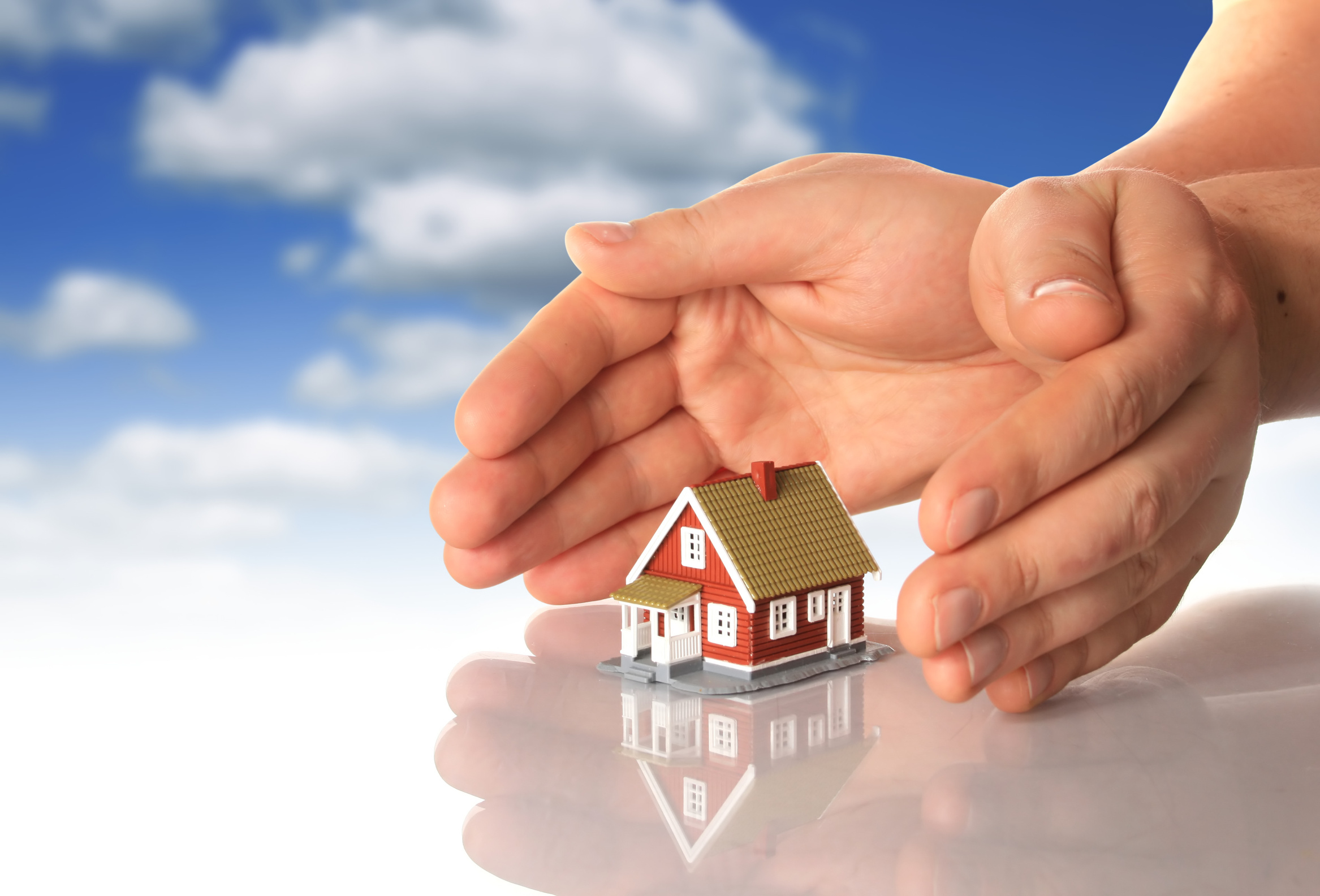 Hands and little house over sky background.